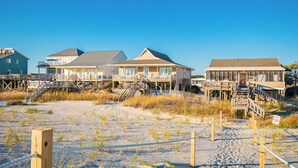 Une propriété située en bord de mer, comprenant plusieurs maisons reliées par des passerelles au-dessus du sable.