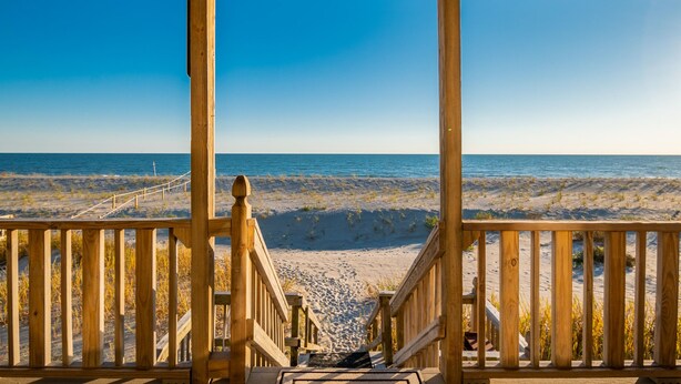 Un escalier en bois menant à une plage, avec un ciel bleu dégagé.