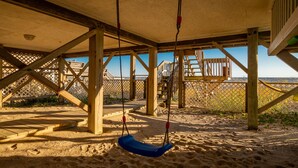 Une balançoire en bois installée sur une plage de sable, avec une terrasse en bois et une vue sur la mer.