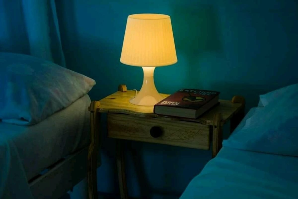 A bedside table with a lamp, a book, and a drawer.