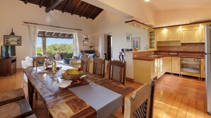 A spacious dining area with a wooden table and chairs, a kitchen with modern appliances, and a view of the outdoors. - Villa Anemelia by Rodostamo Collection (Kassiopi)