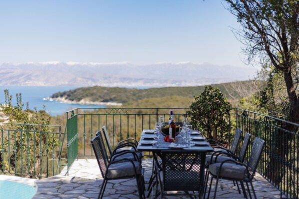 Un espace de restauration en plein air avec une table dressée pour quatre personnes, offrant une vue sur un paysage côtier.