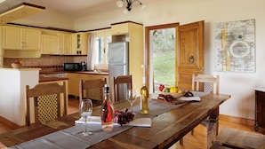 A spacious kitchen with wooden cabinets, a dining table set for two, and a view of the outdoors. - Villa Anemelia by Rodostamo Collection (Kassiopi)