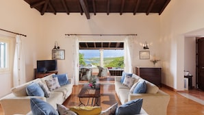 A spacious living room with two sofas, a coffee table, and a television. There is a balcony with a view of the landscape. - Villa Anemelia by Rodostamo Collection (Kassiopi)