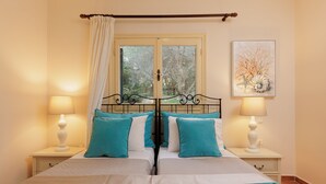 A double bed with a metal frame, two bedside tables with lamps, a window with curtains, and a framed artwork on the wall. - Villa Anemelia by Rodostamo Collection (Kassiopi)