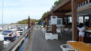 A wooden deck with outdoor seating, overlooking a marina with boats. - Hedone Tróia Resort (Grândola)