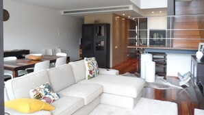 A modern living room with a sectional sofa, a dining table, and a kitchen area with a staircase. - Hedone Tróia Resort (Grândola)