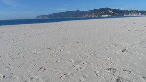 A wide sandy beach with footprints, a clear blue sky, and distant mountains. - Hedone Tróia Resort (Grândola)