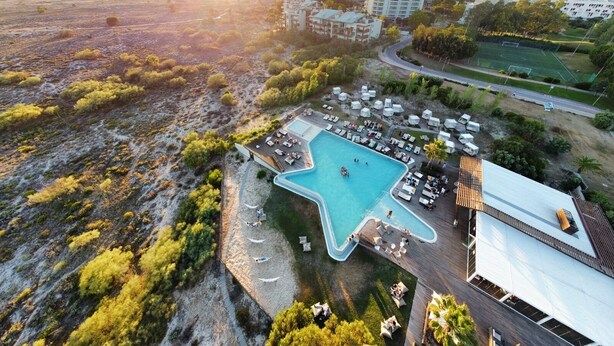 An aerial view of a resort with a large swimming pool, multiple buildings, and a beach area. - Hedone Tróia Resort (Grândola)