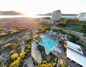 Vista aérea de un complejo turístico con una gran piscina, varias edificaciones y una zona de playa.
