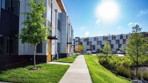Ein modernes Mehrfamilienhaus mit nummerierten Wohnungen, einem gepflegten Rasen und blauem Himmel.