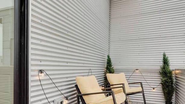 Ein moderner Außenbereich mit zwei Stühlen und einem gemusterten Teppich, einer Holzbalkendecke und einer Metallwand.