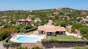 Une villa avec piscine, entourée d’une végétation luxuriante et de collines rocheuses.