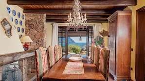 A dining room with a stone wall, a chandelier, and a view of the sea.