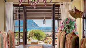 A dining area with a view of a mountainous coastline, a table with a bowl, striped chairs, and a hanging lantern.