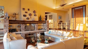 A spacious living room with a stone fireplace, white sofas, and various decorative items on the walls.