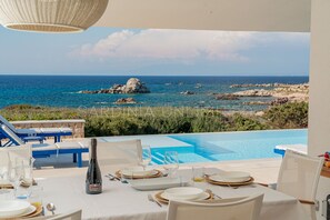 Ein Esstisch, gedeckt für eine Mahlzeit, mit Blick auf das Meer und die felsige Küste.