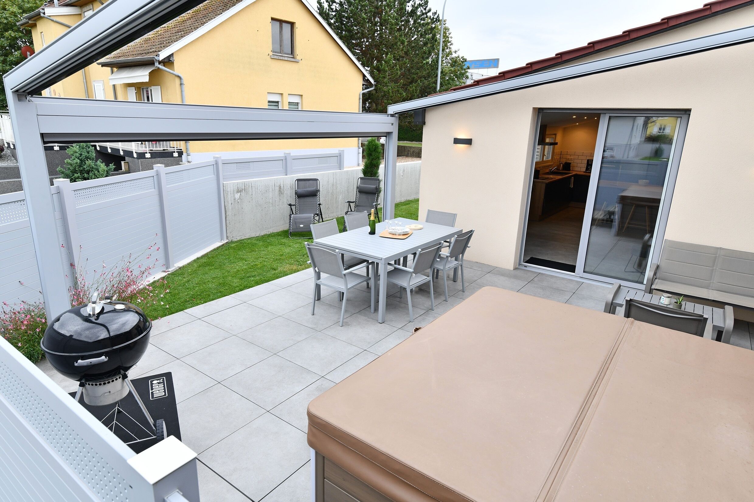 A patio with a barbecue grill, a dining table with chairs, and a covered seating area.