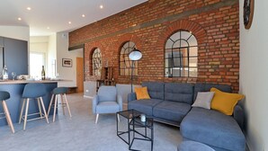 A modern living room with a brick wall, a sofa, a coffee table, and a bar area. - L'Atelier de notre Grand-Père - Jacuzzi (Algolsheim)