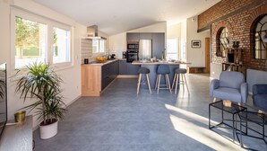A spacious living area with a kitchen, a dining area with bar stools, and a seating area with a chair and a table. - L'Atelier de notre Grand-Père - Jacuzzi (Algolsheim)