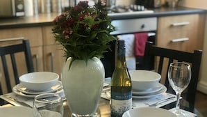 Une table à manger dressée avec de l’assiette blanche, des bols et une bouteille de vin.