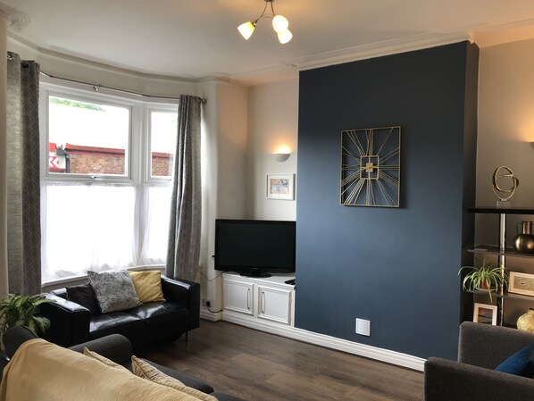 Un salon moderne doté d’un téléviseur à écran plat, d’un mur d’accent bleu foncé et d’un coin salon confortable avec un canapé et un fauteuil.