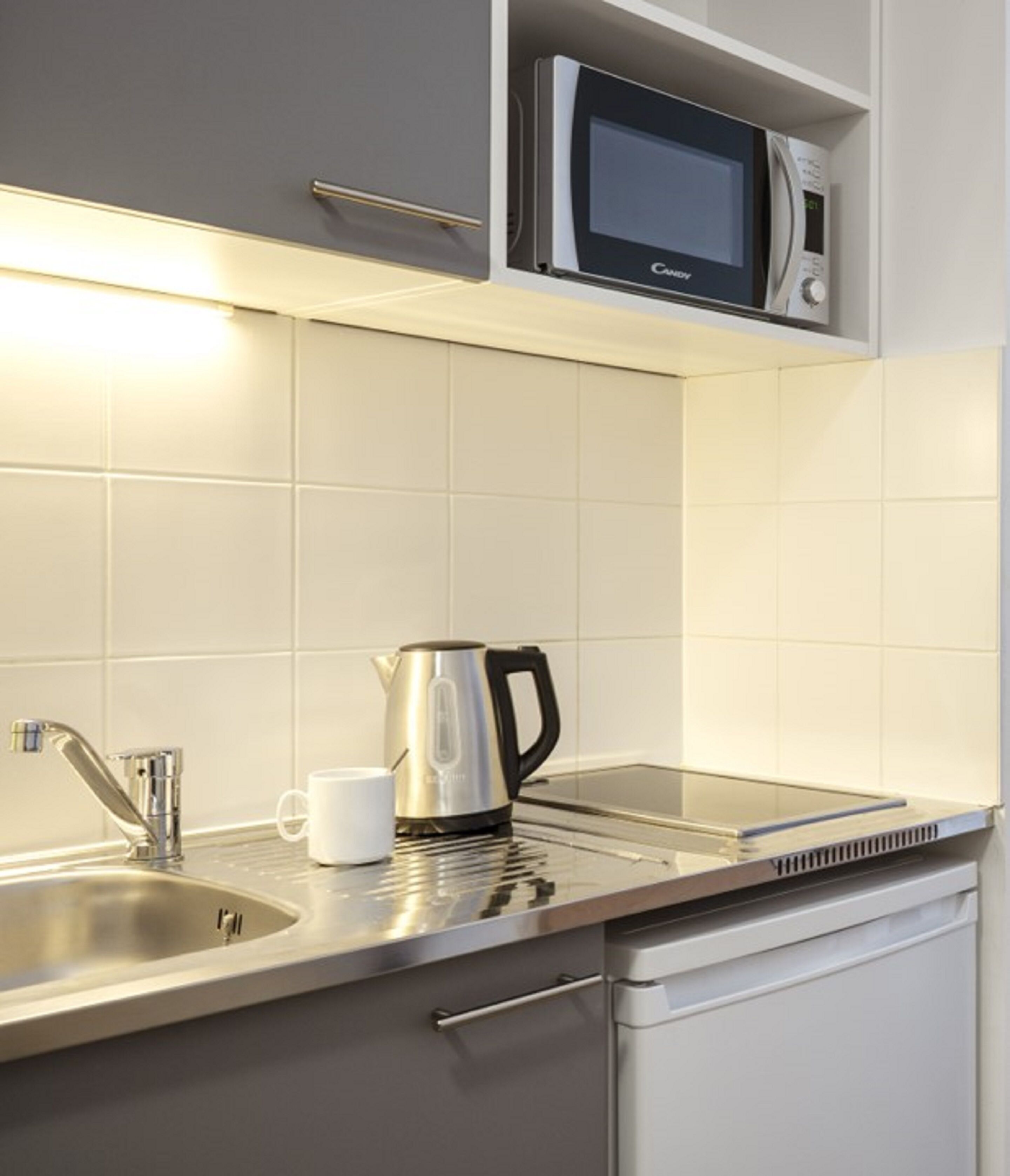A modern kitchen with a stainless steel sink, a kettle, a microwave, and a coffee maker.