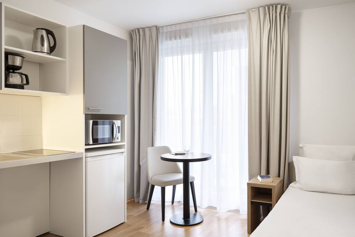 Una habitación de hotel compacta con kitchenette, zona de comedor y cama.