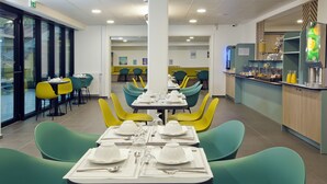 A modern dining area with green and yellow chairs, white table settings, and a counter with food and drinks. - Séjours & Affaires Paris Bagnolet (Bagnolet)