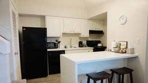 A compact kitchen with white cabinets, a black refrigerator, and a small island with stools.