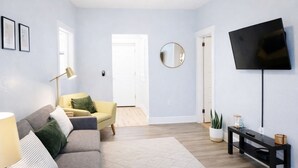 A modern living room with a grey sofa, a yellow armchair, a round mirror, a flat-screen TV, and a small table with decorative items.