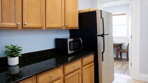 A kitchen with wooden cabinets, a black countertop, a stainless steel refrigerator, and a microwave.