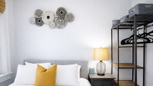 A bedroom with a bed, a bedside table with a lamp, a wall art piece, and a metal wardrobe.