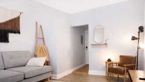A modern living room with a grey sofa, a wooden easel, a small table with a lamp, and a chair. - Downtown Gem • King Bed • Fast WIFI (Salt Lake City)