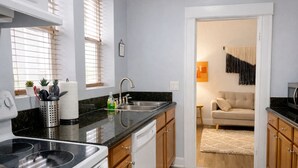 A compact kitchen with a stove, sink, and wooden cabinets. A dining area with a sofa and a rug is visible through an open doorway. - Downtown Gem • King Bed • Fast WIFI (Salt Lake City)
