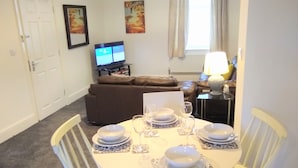 A dining area with a round table set for four, white chairs, and a brown sofa in the background. - Modern Comfy 2-bedroom Flat in St Helens (St Helens)