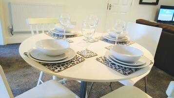 Una mesa de comedor dispuesta con platos, tazones y vasos blancos, rodeada de sillas con manteles individuales de estampado de leopardo.