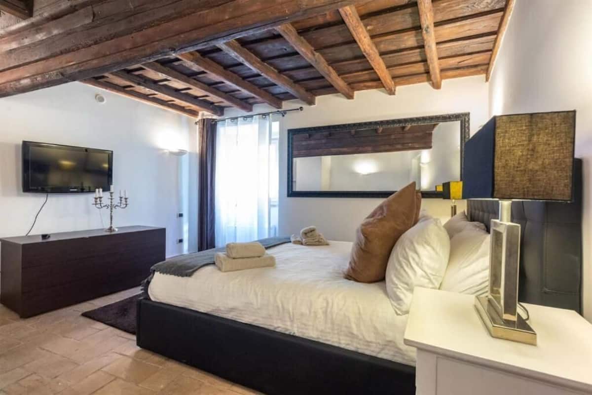 A bedroom with a bed, bedside table, and a TV mounted on the wall.