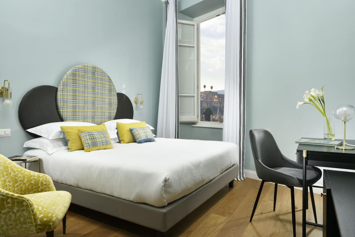 A bedroom with a bed, a desk, a chair, and a view of the city.