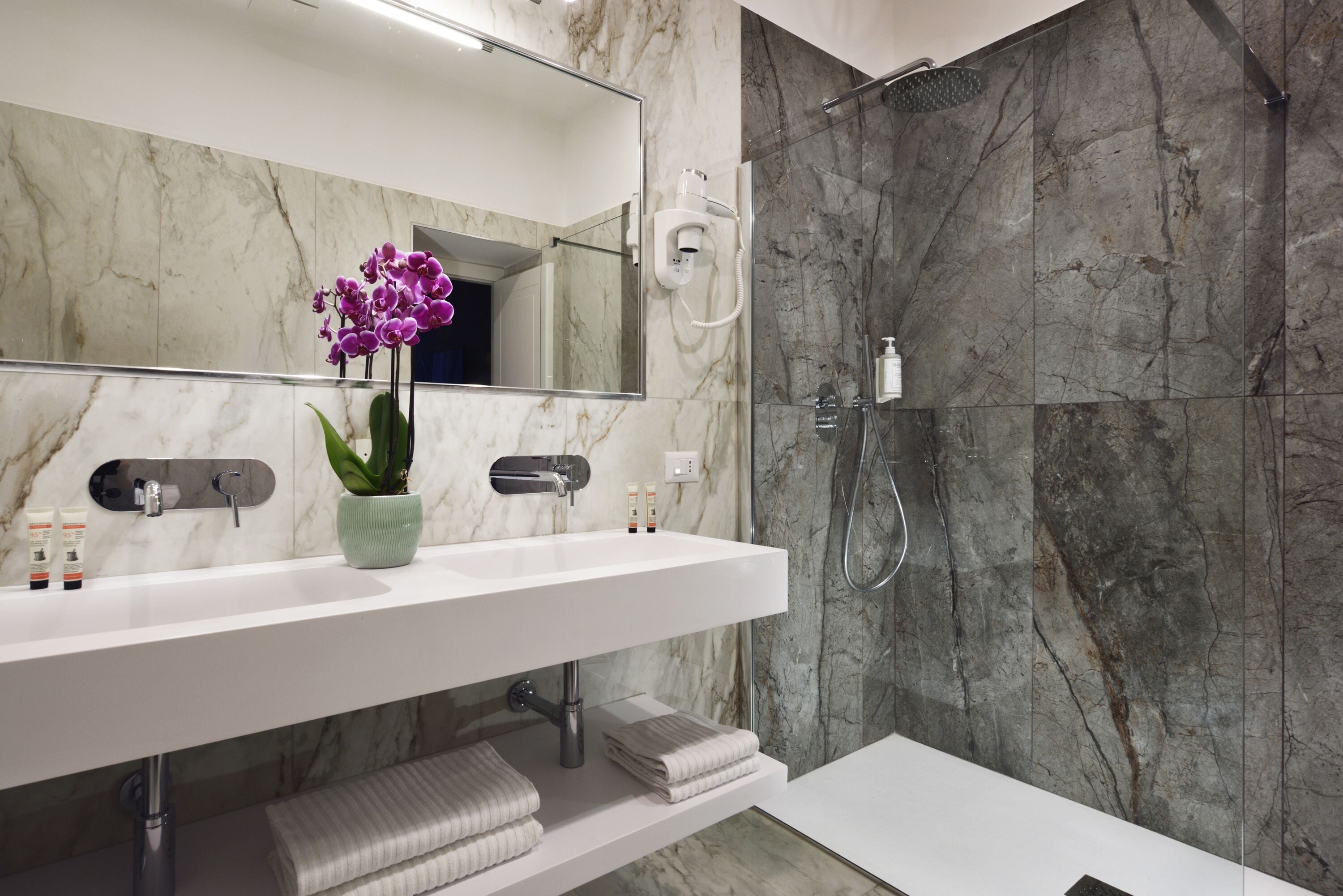 Un bagno moderno con un lavabo in marmo, uno specchio grande, un soffione a mano e un'orchidea in vaso.