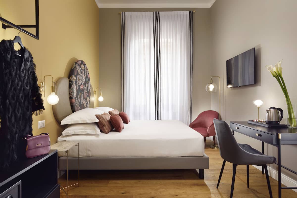 A modern bedroom with a bed, bedside table, chair, and a desk with a lamp.