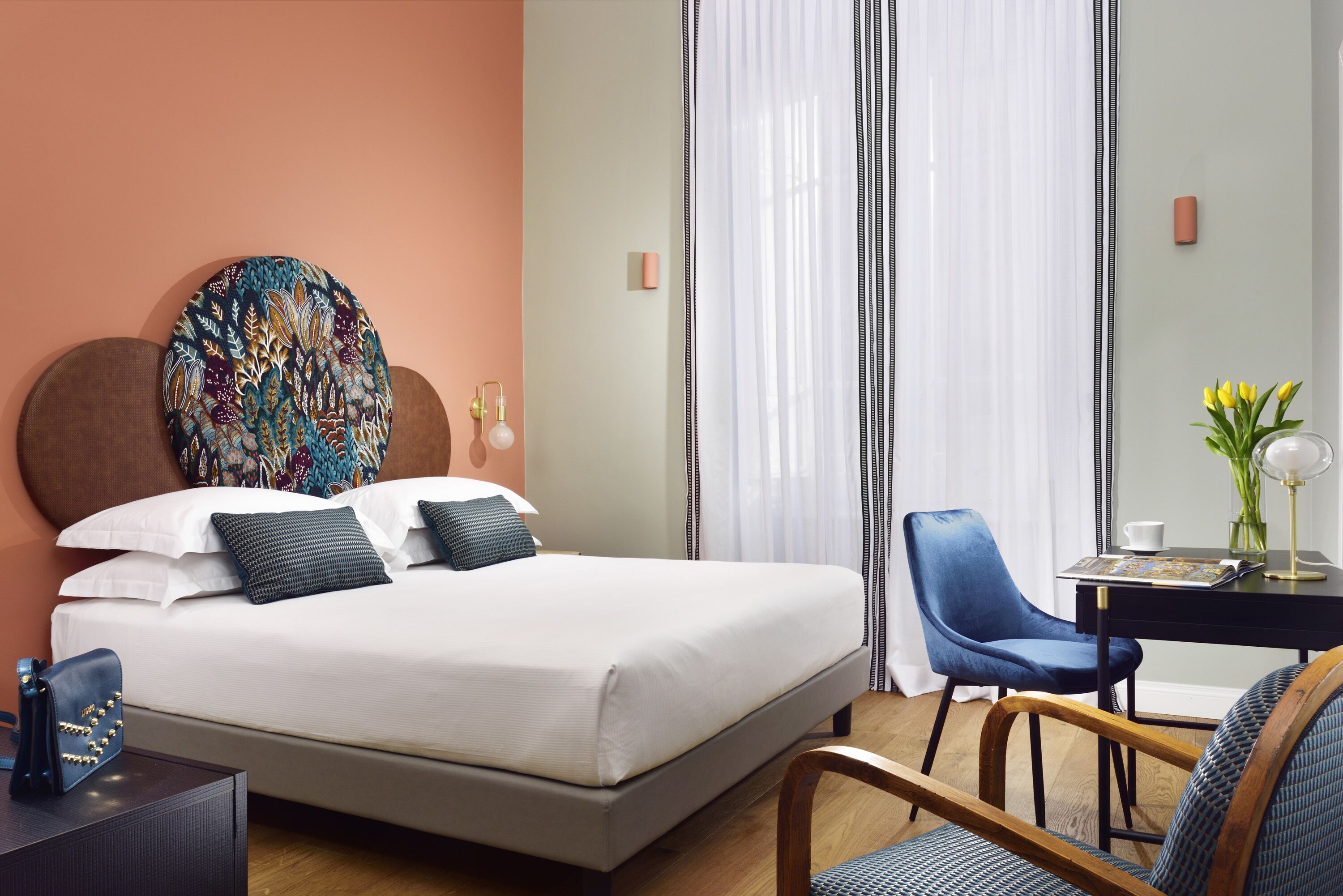 A hotel room with a bed, a desk, a chair, and a window with curtains.