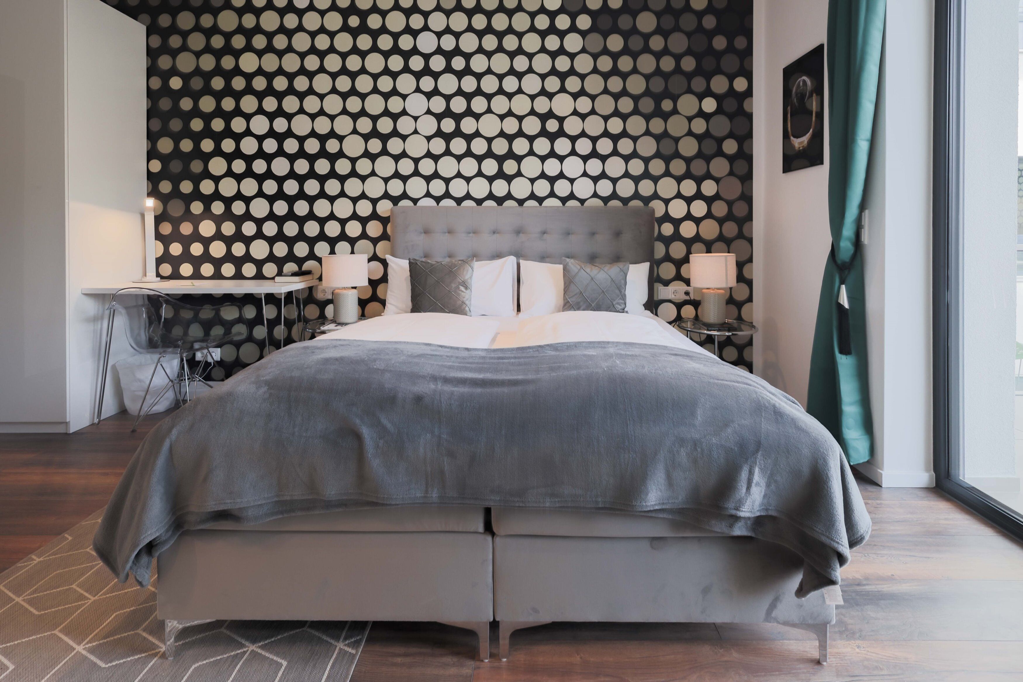 A modern bedroom with a tufted headboard, a grey bedspread, and a patterned wall.