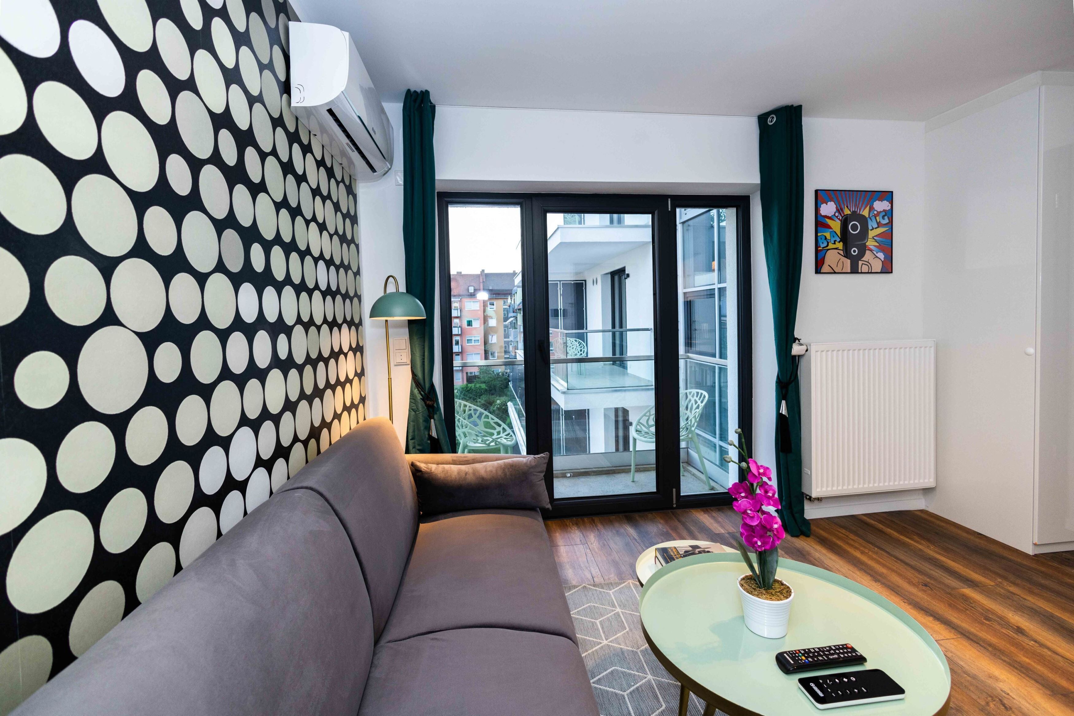 En moderne stue med en grå sofa, et sofabord i glas med en orkidé i potte, og udsigt til byen gennem store glasdøre.