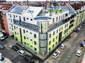 Un bâtiment moderne doté d’une façade originale aux couleurs verte et blanche, de plusieurs étages et d’un toit équipé de panneaux solaires.
