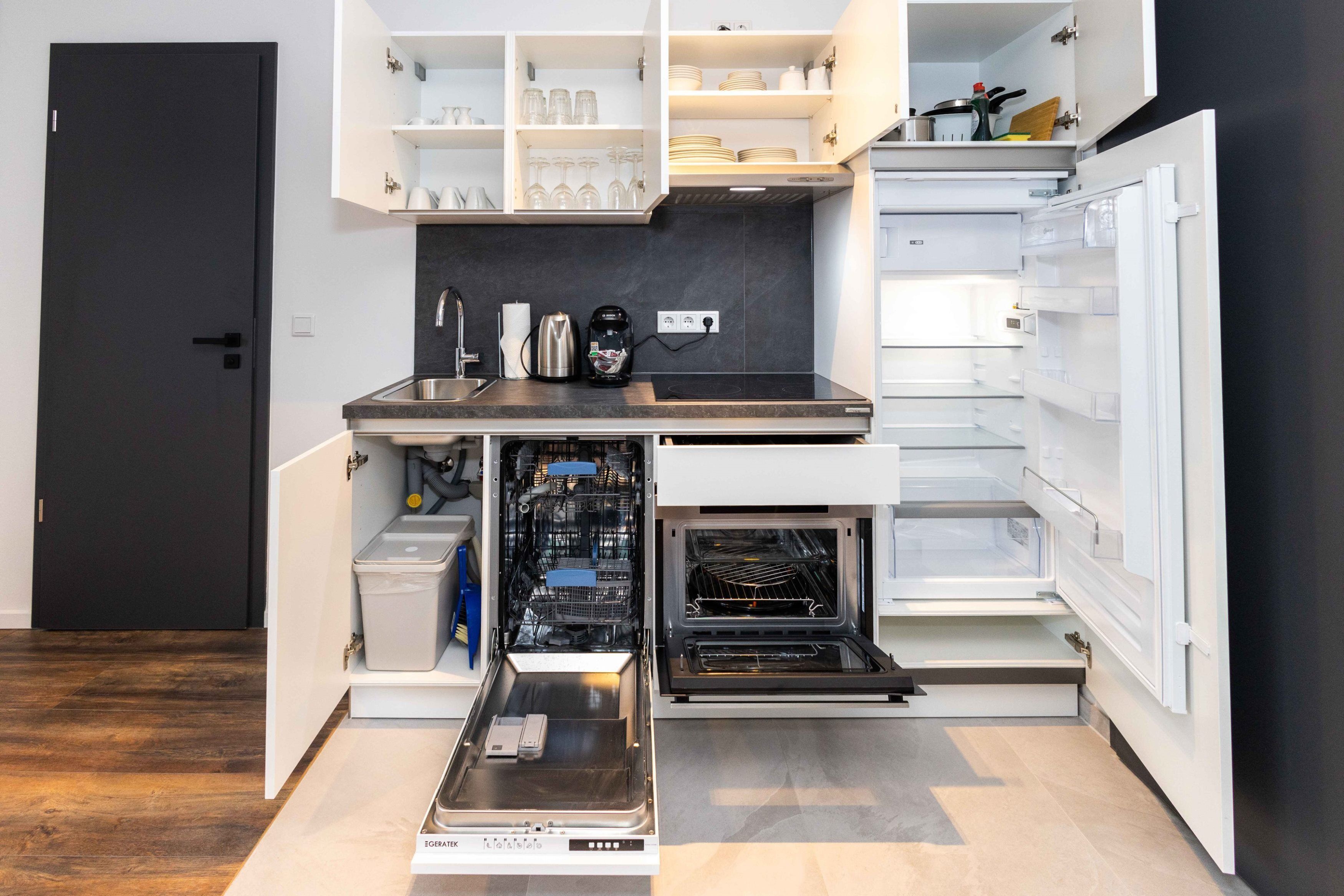 Een compacte keuken met geïntegreerde apparatuur, waaronder een inbouwoven en een koffiezetapparaat.