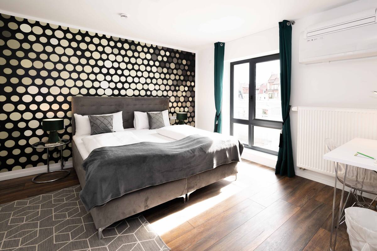Ein modernes Schlafzimmer mit Bett, Nachttisch, Lampe, einem Fenster mit Vorhängen und einer Heizung.