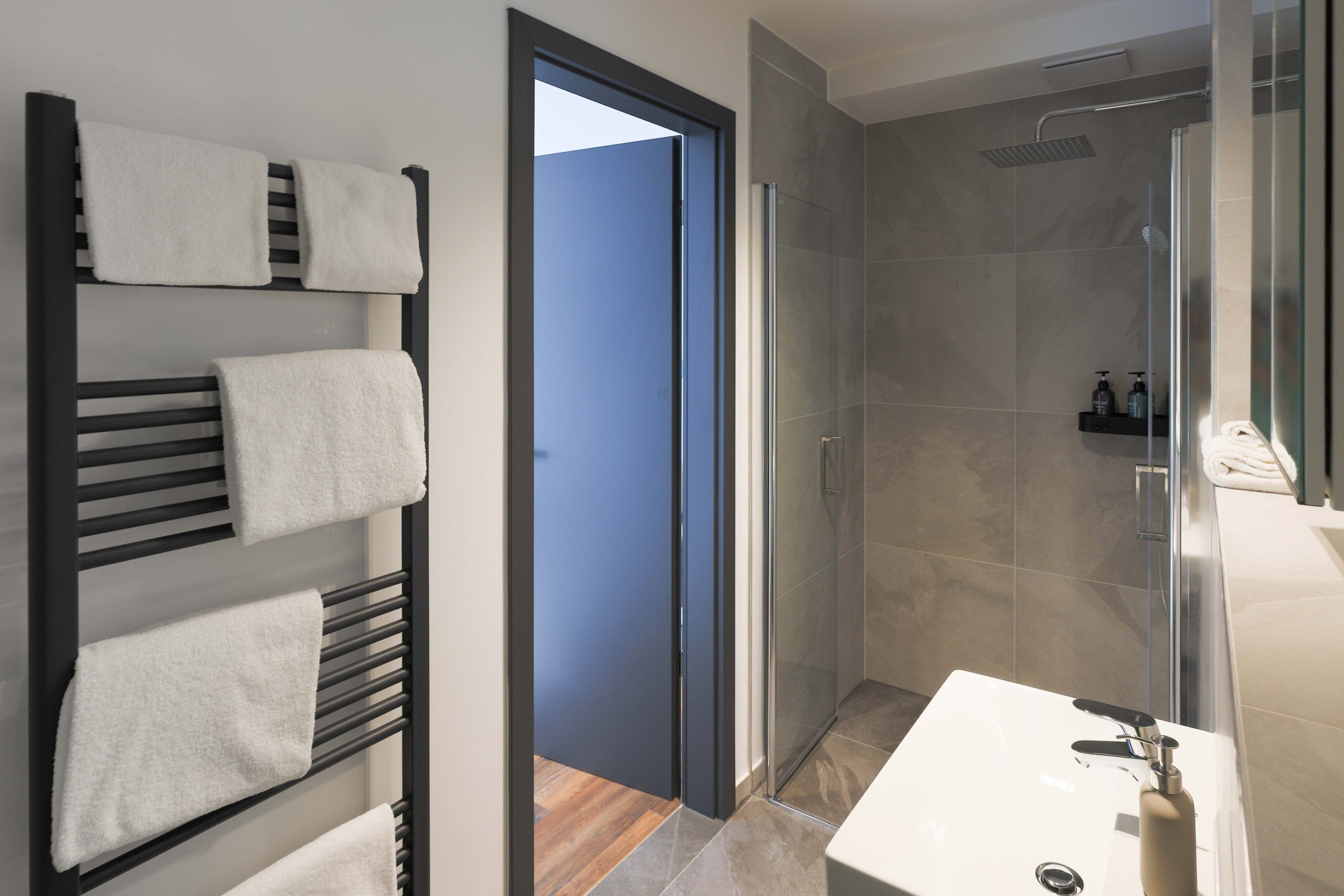 A modern bathroom with a glass shower, a white sink, and a towel rack with multiple towels.