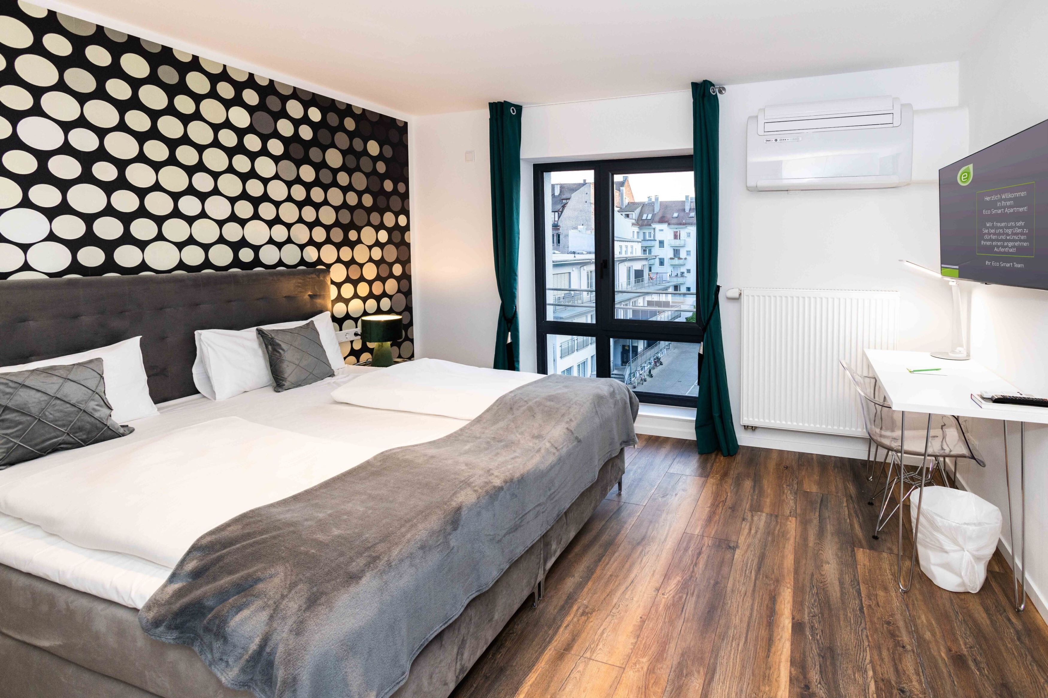 Ein modernes Hotelzimmer mit einem großen Bett, einem Schreibtisch und Blick auf die Stadt durch ein Fenster.