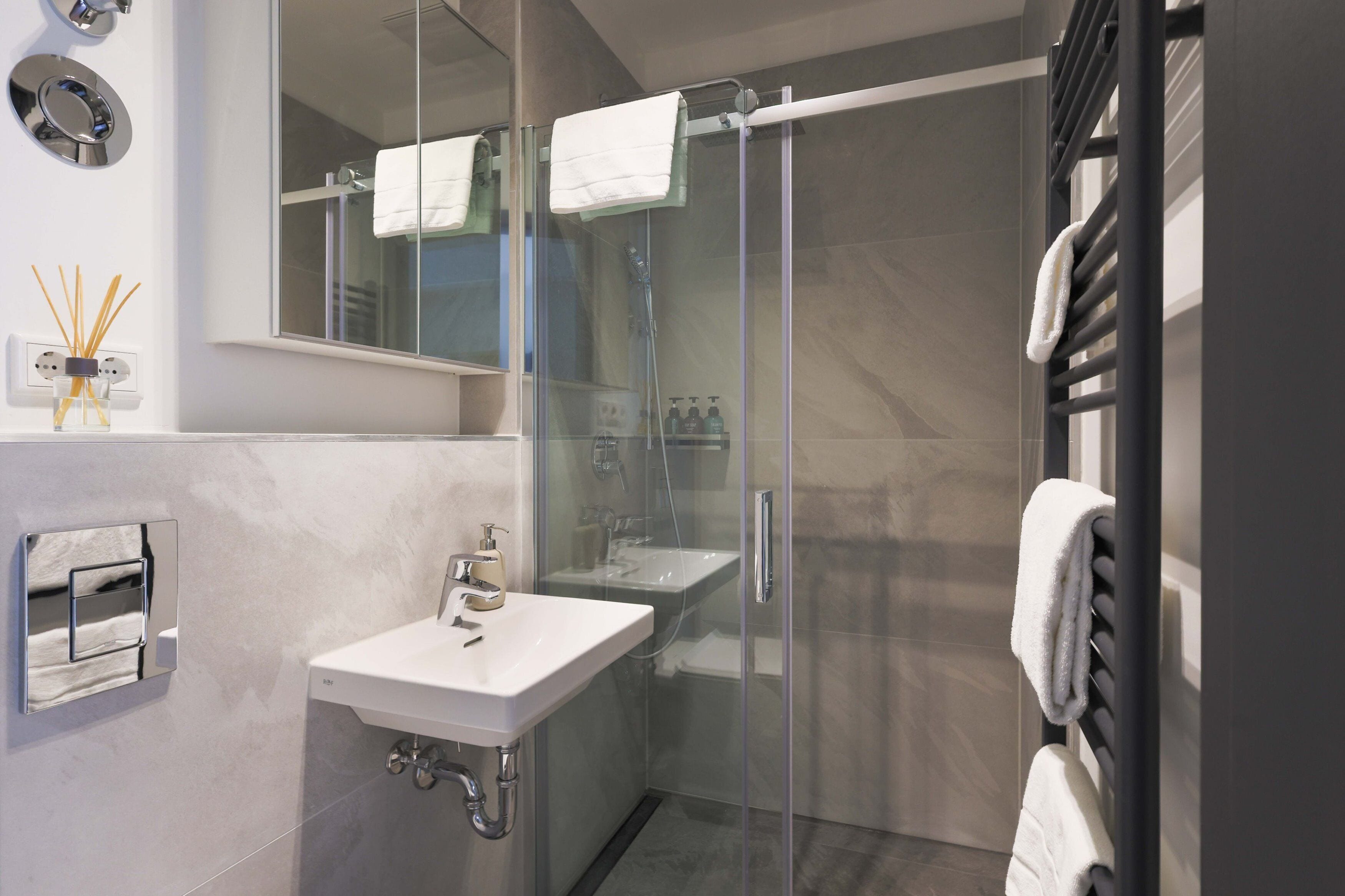 Un baño moderno con ducha de vidrio, lavamanos blanco y toallero.